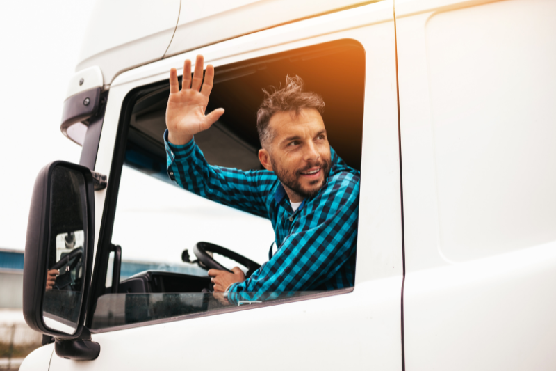 Un șofer face cu mâna dintr-un camion alb