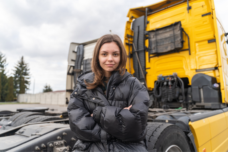 O doamnă stă cu mâinile încrucișate în fața unui camion galben.